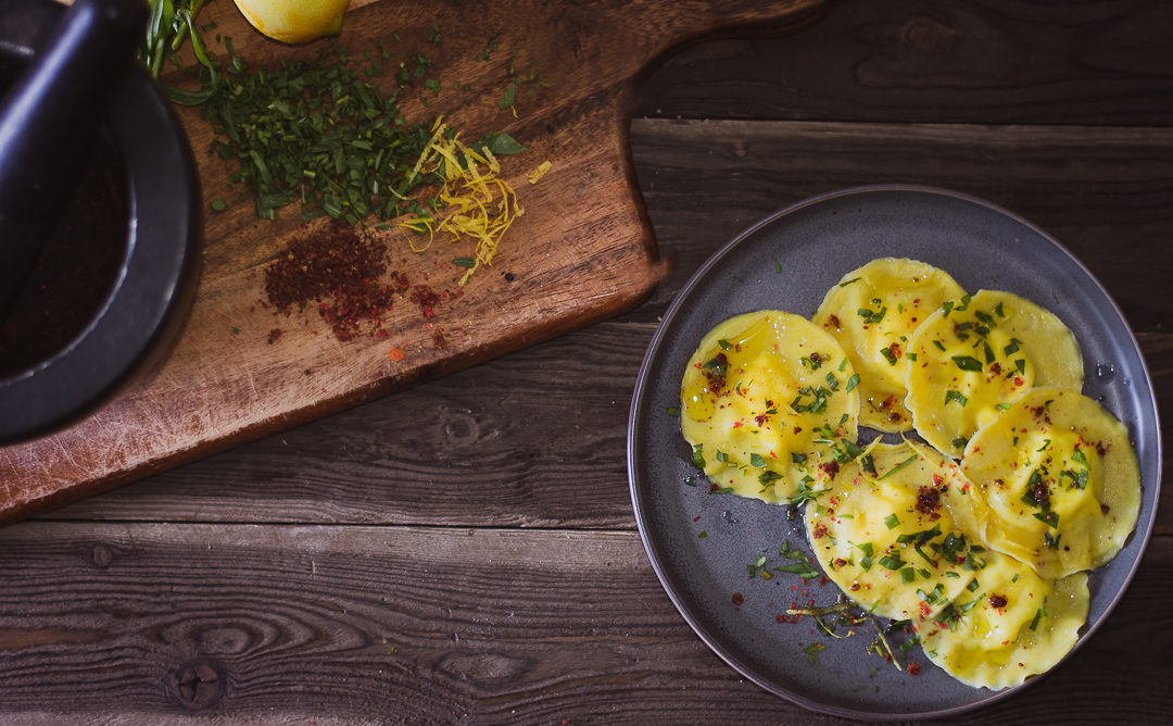 Lemon goat cheese ravioli on plate with tarragon and pink peppercorn on cutting board